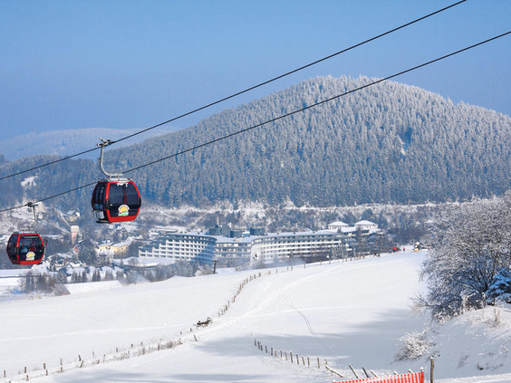 De Ettelsberg-kabelbaan met rode gondels die boven het besneeuwde winterlandschap van Willingen in Sauerland zweven.