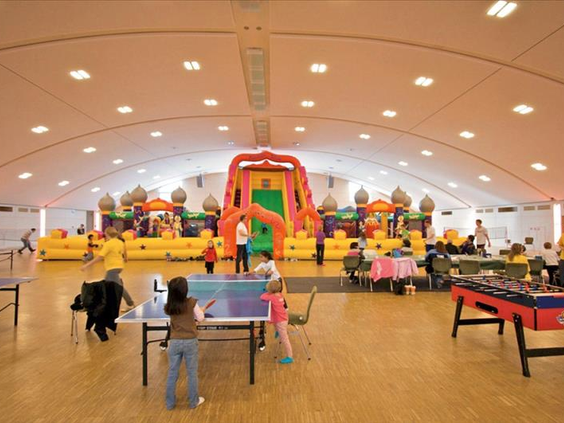Kinderen spelen tafeltennis en vermaken zich op de springkussens in de grote speelhal van het Kinderparadijs in Hotel Sauerland Stern.