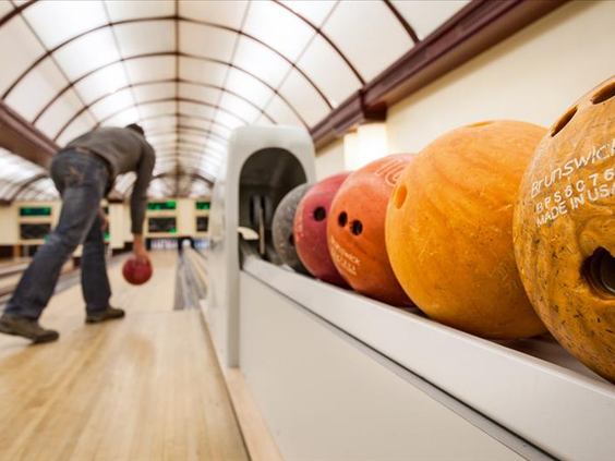 Iemand gooit een bowlingbal op een van de bowlingbanen in Hotel Sauerland Stern, met andere ballen op de voorgrond.
