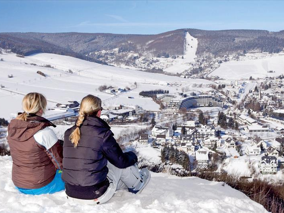 Twee wintersporters genieten van het panoramische uitzicht over het besneeuwde dorp Willingen vanaf de top van een berg in Sauerland.