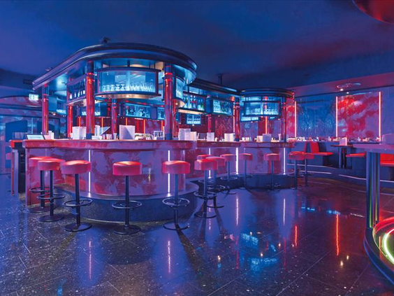 De lege, trendy en modern verlichte discotheek 'Star Club' in Hotel Sauerland Stern, met een grote bar en rode barkrukken.