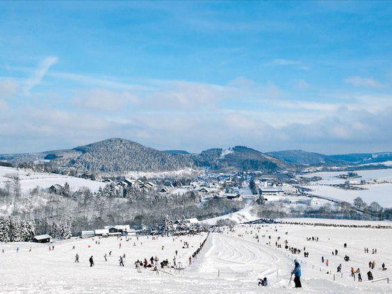 Weids overzicht van het kindvriendelijke skigebied van Willingen in Sauerland, met veel skiërs op de besneeuwde pistes onder een strakblauwe lucht.