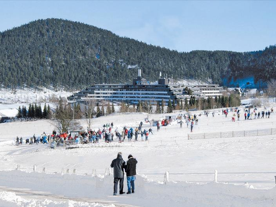 Uitzicht op het grote Hotel Sauerland Stern, gelegen aan de piste in een besneeuwd landschap in Willingen, met wintersporters op de voorgrond.