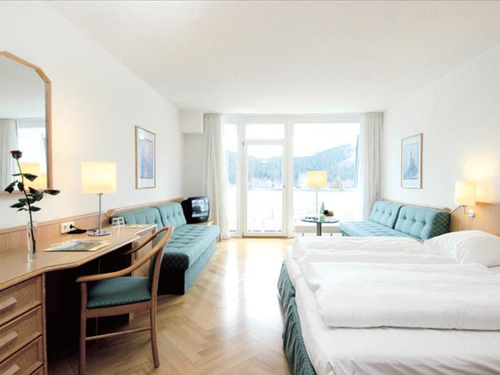Lichte en ruime familiekamer in Hotel Sauerland Stern met comfortabele bedden, een bureau en een groot raam met uitzicht op het winterlandschap.