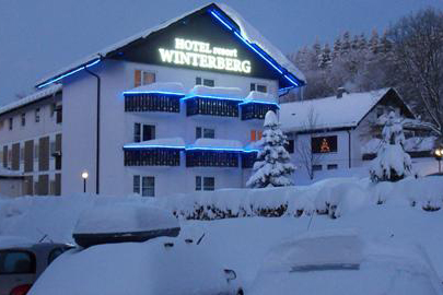 De buitenkant van het sfeervol verlichte Hotel Winterberg Resort in de avond, omringd door een dik pak sneeuw.