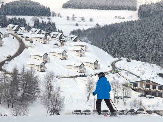 Een skiër op de piste kijkt uit over het besneeuwde dorp en de vakantiehuizen van Winterberg.