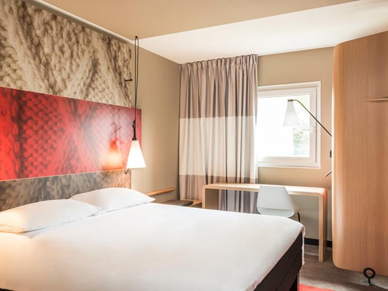 Een comfortabele en moderne hotelkamer in het Ibis Hotel in Aken, met een groot tweepersoonsbed en een rood hoofdeinde.