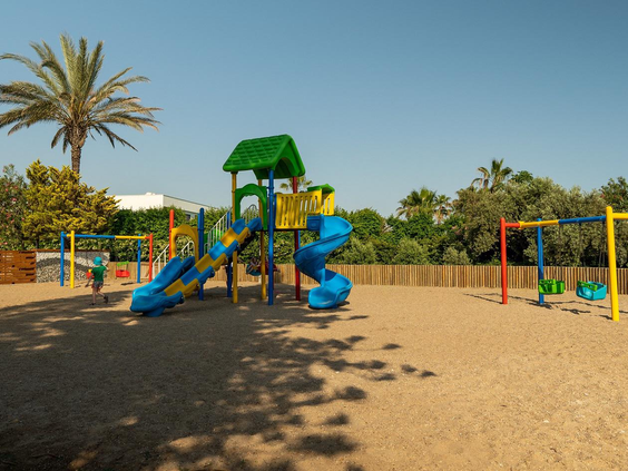 De leuke buitenspeeltuin van hotel Pegasos World in Side, Turkije, met een klimtoestel, glijbanen en schommels in het zand.