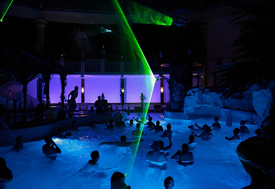 Bezoekers in het zwembad tijdens het discozwemmen, met spectaculaire paarse en blauwe verlichting en een groene lasershow.