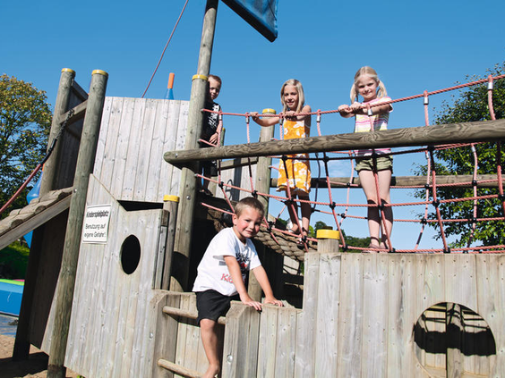 Kinderen klimmen en spelen op een groot houten piratenschip in de buitenspeeltuin van Eifelpark Kronenburger See.