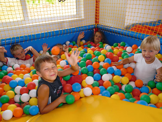 Vrolijke kinderen spelen en duiken in de kleurrijke ballenbak van de indoorspeeltuin op Eifelpark Kronenburger See.