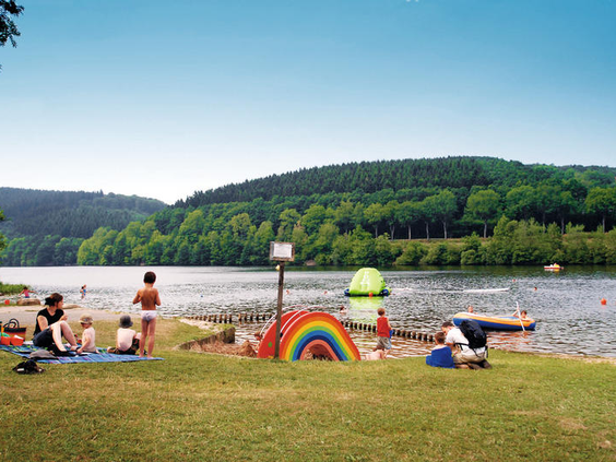 Gezinnen met kinderen genieten van de zon op het zandstrand aan de oever van de Kronenburger See, vlak bij het vakantiepark.