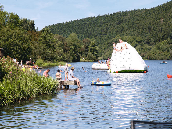 Kinderen en volwassenen spelen op de opblaasbare waterspeeltuin met een grote klimijsberg op de Kronenburger See.