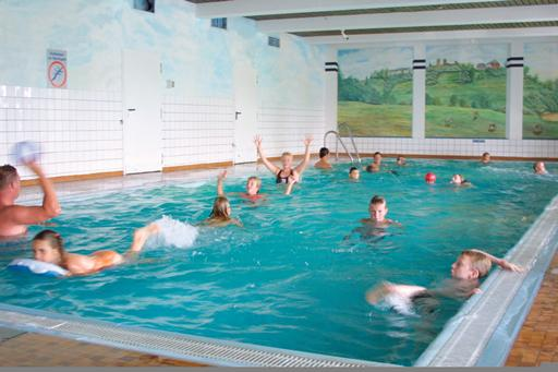 Een groep kinderen en tieners heeft plezier en speelt in het helderblauwe water van het binnenzwembad op het vakantiepark.