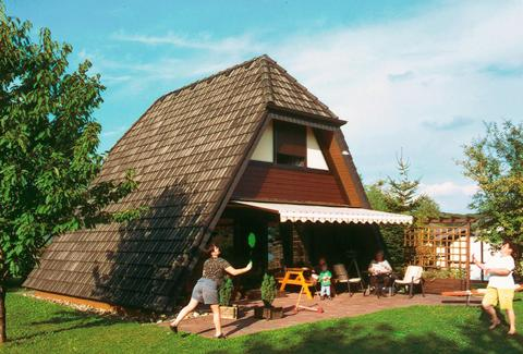 Een A-frame vakantiehuisje op Feriendorf Waldbrunn in het Zwarte Woud, met een familie die ontspant en badmintont op het terras.
