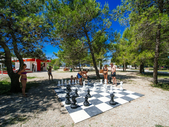 Gasten spelen op een reusachtig schaakbord in de schaduw van pijnbomen op het kindvriendelijke Zaton Holiday Resort in Kroatië.