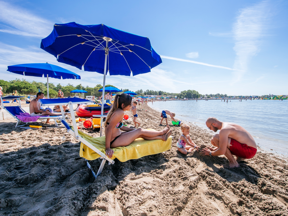 Gezin met een jong kind bouwt zandkastelen op het langzaam aflopende zandstrand van het kindvriendelijke Zaton Holiday Resort in Kroatië.