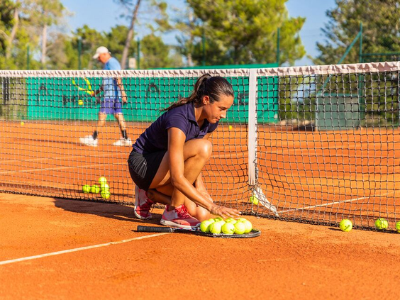 Een jonge vrouw krijgt tennisles en raapt ballen op de gravel tennisbaan van Zaton Holiday Resort, ideaal voor een sportieve vakantie.