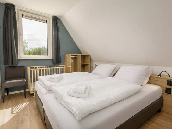 Modern ingerichte slaapkamer in een vakantiehuis op Vakantiepark Sandur met een opgemaakt tweepersoonsbed en een kinderbedje.