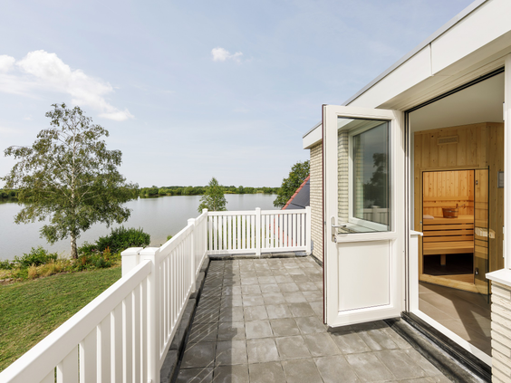 Het terras van een wellness vakantiehuis aan het water op Vakantiepark Sandur, met uitzicht op de Grote Rietplas en een buitensauna.