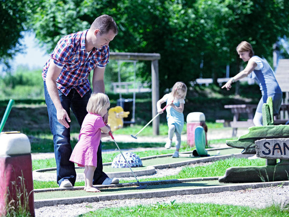 Gezin met jonge kinderen speelt een potje midgetgolf op de midgetgolfbaan van Vakantiepark Sandur.