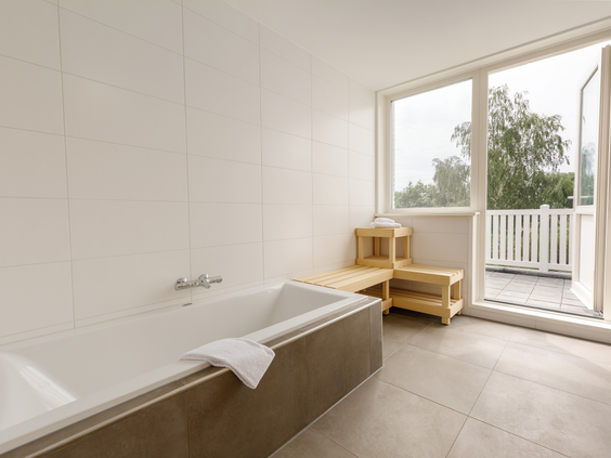 Ruime en lichte badkamer in een vakantiehuis op Vakantiepark Sandur, met een groot ligbad en uitzicht naar buiten.