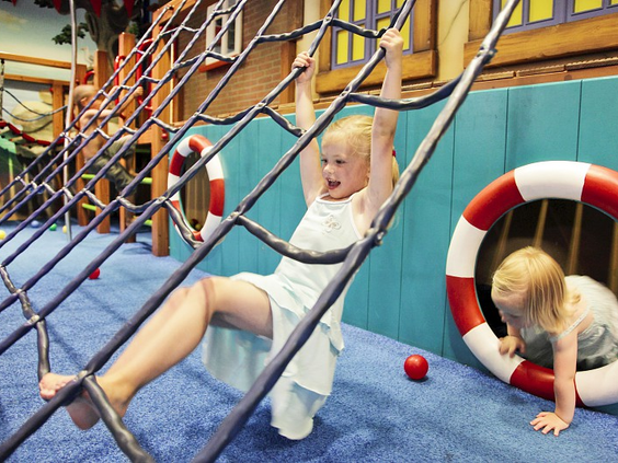 Meisje klimt en klautert in het indoor speelparadijs met netten en obstakels op Vakantiepark Sandur.