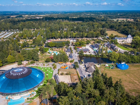 Luchtfoto van het uitgestrekte vakantiepark Domaine des Ormes in Bretagne, Frankrijk, met het grote overdekte waterpark, diverse zwembaden, het kasteel en de groene omgeving.