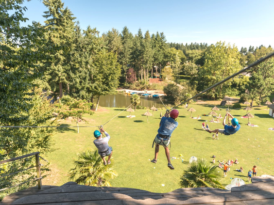 Kinderen op de zipline in het avontuurlijke klimpark van camping Domaine des Ormes, een topactiviteit voor een actieve familievakantie in Frankrijk.