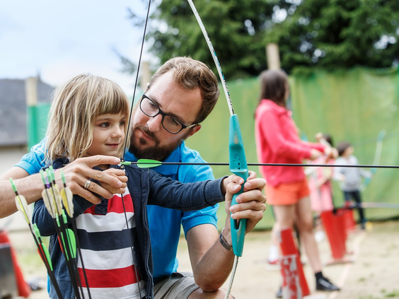 Vader helpt zijn zoon met pijl en boog bij het boogschieten op de kindvriendelijke camping Domaine des Ormes in Frankrijk.