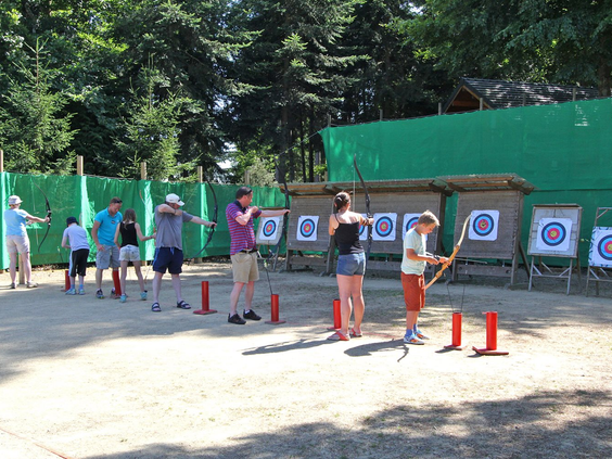 Groep kinderen en volwassenen krijgen instructies bij de boogschietbaan op de kindvriendelijke camping Domaine des Ormes.