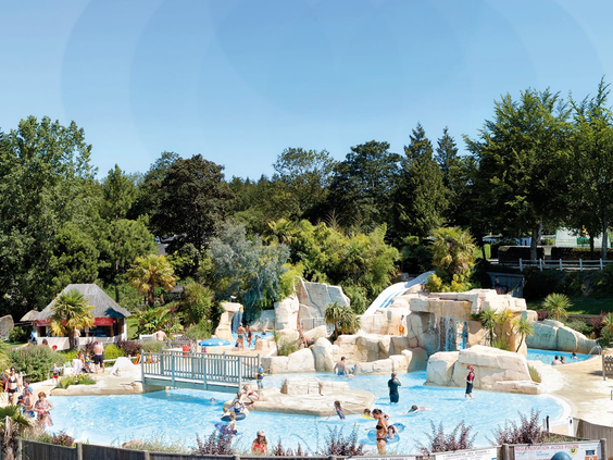 Het lagune zwembad in het buitenwaterpark van Domaine des Ormes, met rotsformaties, watervallen en veel zwemmende gezinnen op een zonnige dag.