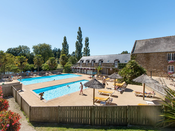 Een rustiger, omheind zwembad op camping Domaine des Ormes, omringd door ligbedden en parasols, direct gelegen bij de appartementen.