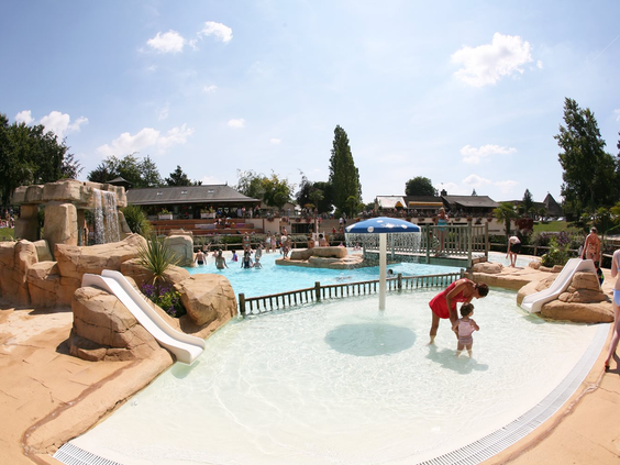 Het ondiepe kinder- en peuterbad op Domaine des Ormes, met kleine glijbaantjes en een paddenstoelfontein waar een ouder met een kind speelt.