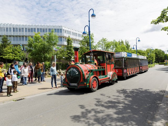 Rood toeristentreintje rijdt langs de weg bij vakantiepark Park Nordseeküste, met gezinnen die wachten om in te stappen.