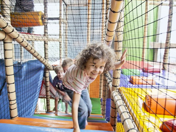 Lachend meisje klimt en klautert door de netten in de kleurrijke overdekte indoorspeeltuin van Park Nordseeküste.