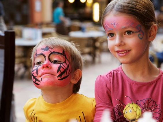 Twee kinderen met vrolijk geschminkte gezichten, als spin en met glitter, tijdens de kinderanimatie in Park Nordseeküste.