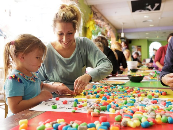 Moeder en dochter zijn samen creatief aan het knutselen met kleurrijke materialen aan een grote tafel in de kidsclub.