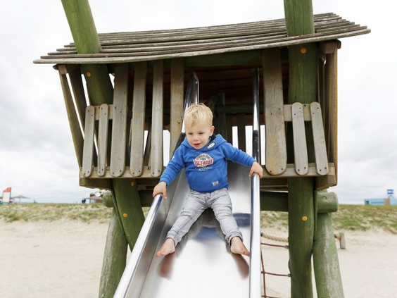 Jonge peuter zit bovenaan een houten glijbaan in de buitenspeeltuin op het vakantiepark.