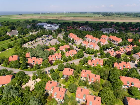 Luchtfoto van het ruim opgezette en groene vakantiepark Park Nordseeküste in Tossens, met de vakantiehuisjes en de Noordzee aan de horizon.