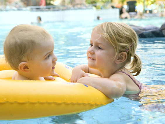 Een baby en een peuter spelen veilig samen met een gele zwemband in het ondiepe kindergedeelte van het zwembad.