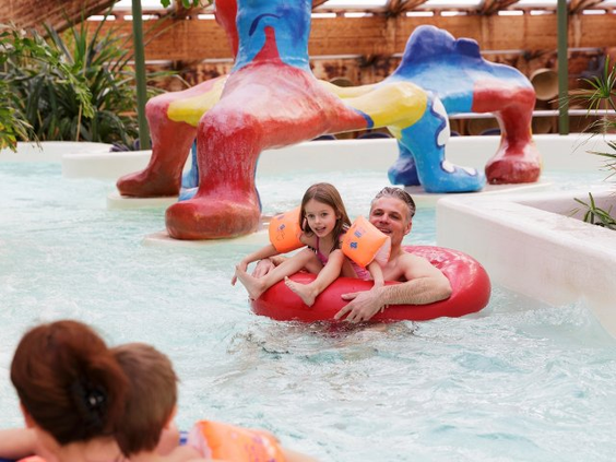 Vader en dochter dobberen vrolijk in een grote rode band door een stroomversnelling of lazy river in het zwemparadijs.
