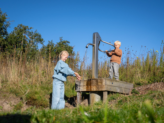 Twee kinderen spelen met een ouderwetse waterpomp in een natuurlijke omgeving op Kustpark Texel.