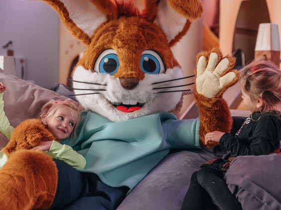 Twee blije meisjes geven een dikke knuffel aan de grote, vrolijke parkmascotte.