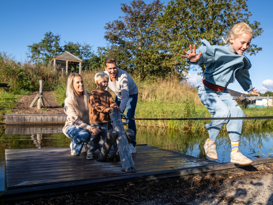 Gezin met kinderen en hond heeft plezier op een houten trekvlot bij het water op Kustpark Texel.