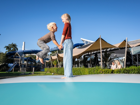 Twee kinderen springen hand in hand op de grote airtrampoline op Kustpark Texel.