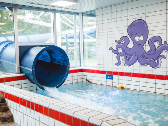 Blauwe kinderglijbaan die uitkomt in het peuterbad met een octopus op de muur in zwemparadijs Caluna.