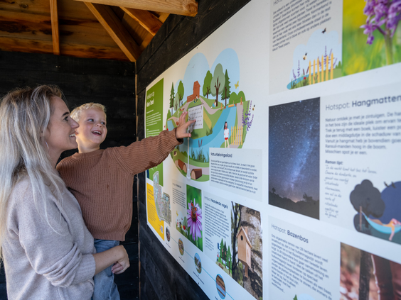 Moeder en kind kijken naar een informatiebord over de natuur op vakantiepark Kustpark Texel.