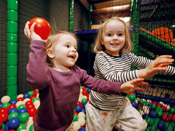 Twee vrolijke peuters die spelen met rode ballen in de kleurrijke ballenbak van Monky Tonky Land.
