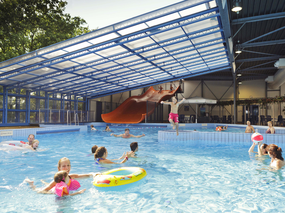 Overzicht van het binnenzwembad met uitschuifbaar dak op Landal het Land van Bartje, waar kinderen en volwassenen zwemmen en spelen in het water.